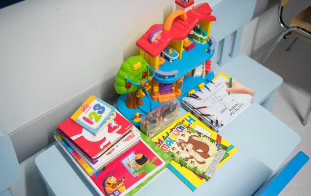 Mały bialy stolik na korytarzu Oddziału Chorób Dziecięcych. Na stoliku leżą książeczki i zabawki dla mniejszych dzieci.