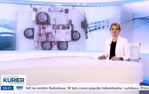 Zrzut ekranu programu telewizyjnego Telewizyjny Kurier Warszawski. Na pierwszym planie prezenterka siedzi przy białym stole w studio i prezentuje wiadomości