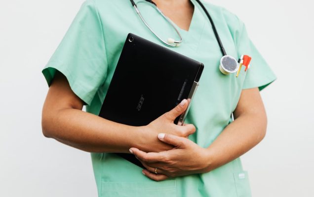 Niepełne ujęcie pielęgniarki trzymającej w rękach tablet, na szyi stetoskop.