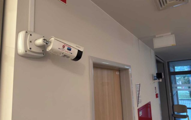 System do pomiaru temperatury, zainstalowany przy drzwiach oznaczony nalepkami logotypów projektu.