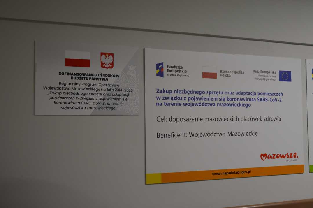 Dwie tablice z informacją o projekcie przyczepione obok siebie na ścianie korytarza szpitala.