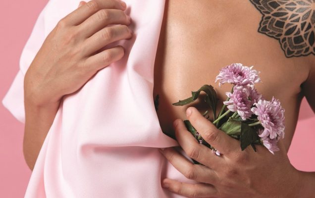 fragment sylwetki kobiety trzymającej w jednej dłoni różowe kwiaty i odsłaniającej lekko pierś