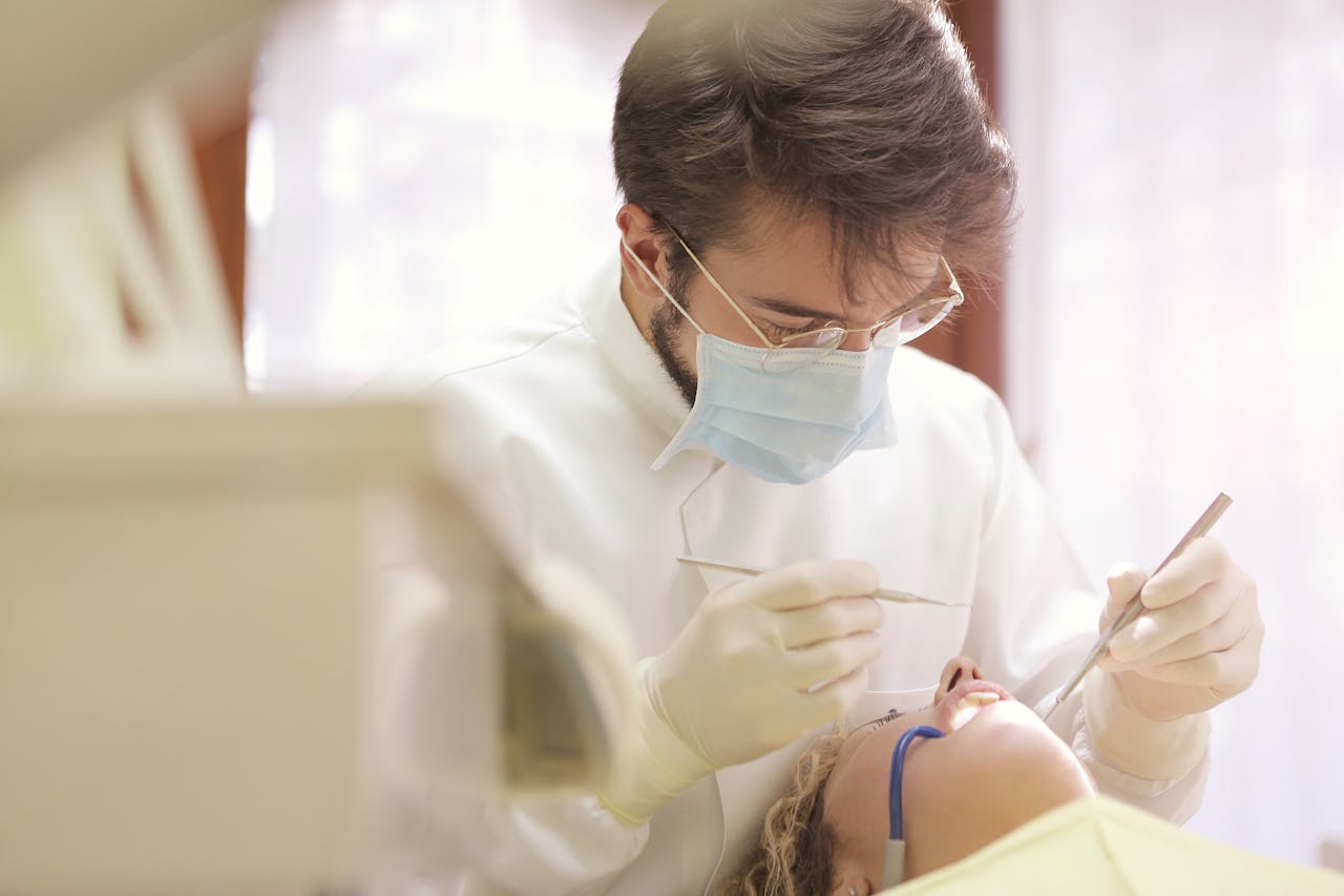 Dentysta w gabinecie zagląda do jamy ustnej pacjenta, w ręku trzyma narzędzia dentystyczne