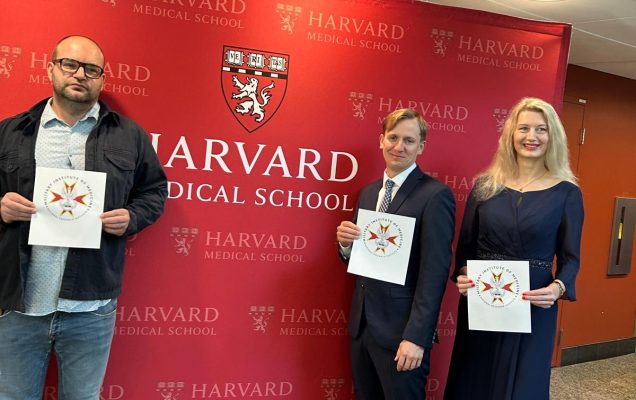 Naukowcy z dyplomami na tle czerwonej ścianki medialnej Harvard Medical School.