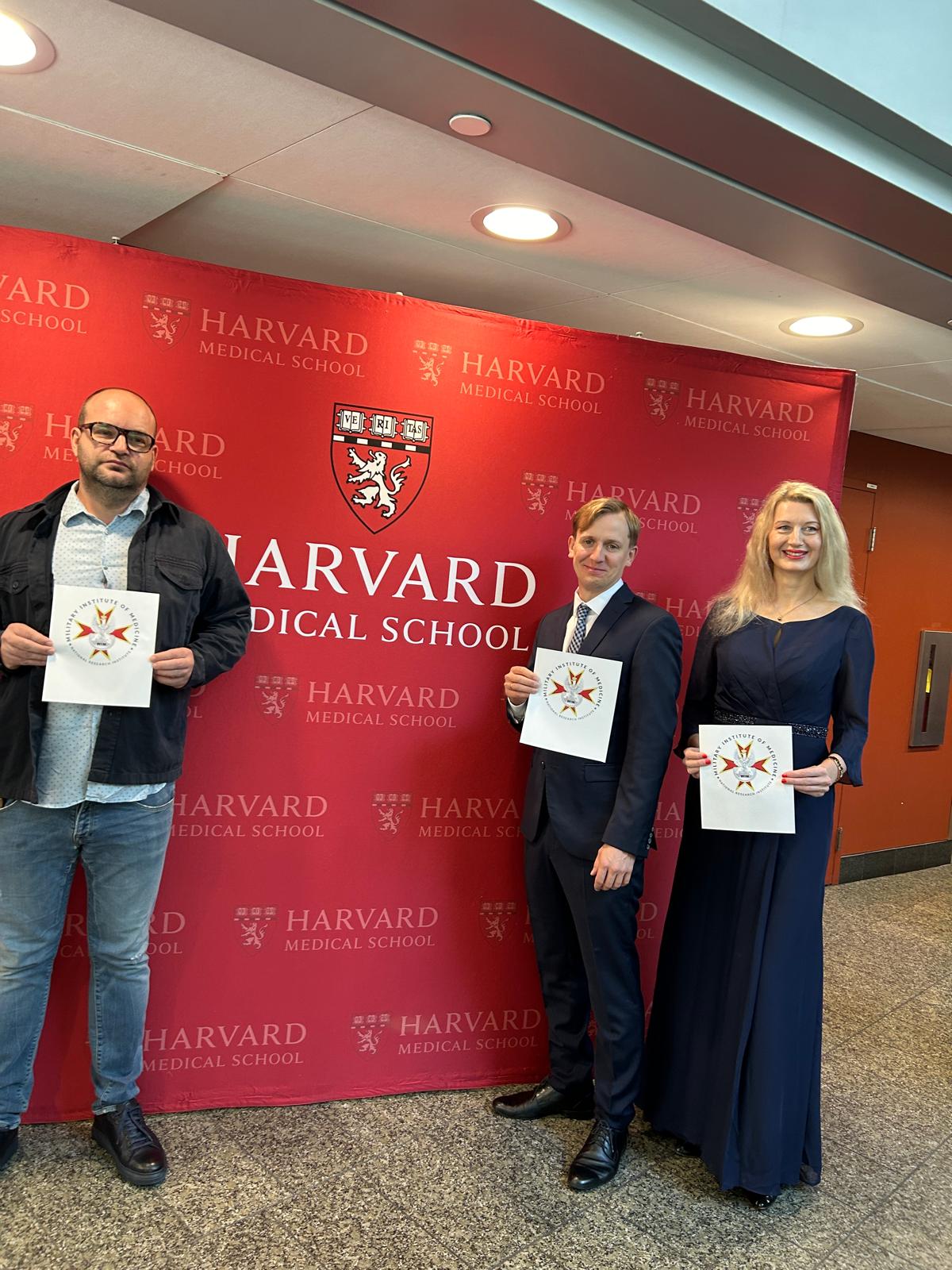 Naukowcy z dyplomami na tle czerwonej ścianki medialnej Harvard Medical School.