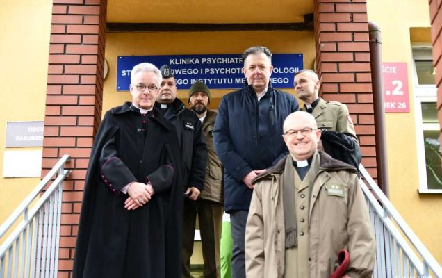 Biskup polowy Wiesław Lechowiczem podczas spotkania z pracownikami Kliniki Psychiatrii, Stresu Bojowego i Psychotraumatologii Wojskowego Instytutu Medycznego w Warszawie. Biskup i profesor Tworus ubrani w zimowe kurtki stoją na schodach Kliniki z pracownikami.