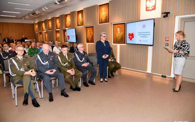 Małgorzata Złotkowska prowadzi uroczystość w Wojskowym Instytucie Medycznym. W tle uczestnicy uroczystości.