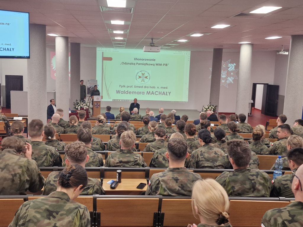 Lekarze w wojskowych mundurach siedzą na auli podczas konferencji.