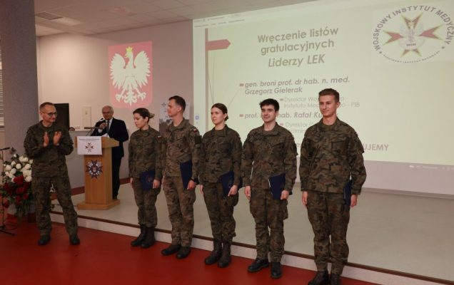 Wyróżnieni lekarze wojskowi pozują do zdjęcia. Z lewej strony Dyrektor WIM-PIB klaszcze w dłonie.