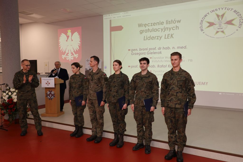 Wyróżnieni lekarze wojskowi pozują do zdjęcia. Z lewej strony Dyrektor WIM-PIB klaszcze w dłonie.