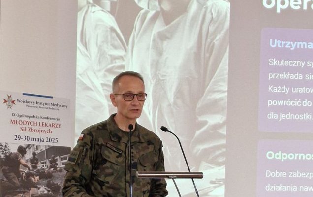 Dyrektor WIM-PIB w mundurze wojskowym przy mównicy. Za nim wyświetlony obraz z prezentacji lekarza w maseczce chirurgicznej.