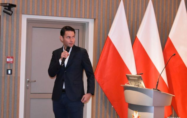 Prelegent konferencji z mikrofonem w dłoni.