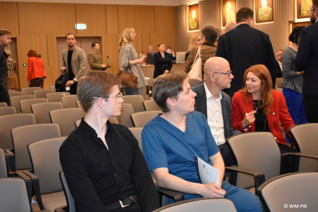 Fragment auli podczas przerwy. Na pierwszym planie 2 siedzących lekarzy, jeden z nich ubrany w strój chirurgiczny.