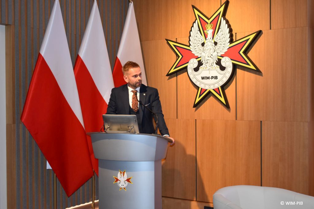 Prelegent przy mównicy podczas konferencji.