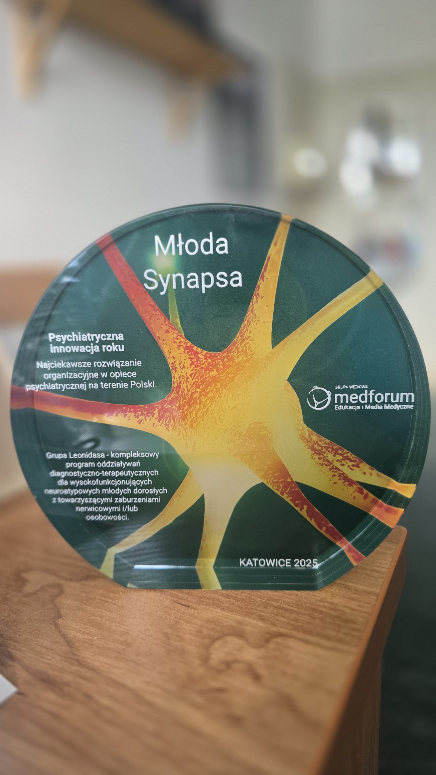 Nagroda Młoda Synapsa. Forma owalna w środku na zielonym tle żółto-pomarańczowy neuron.