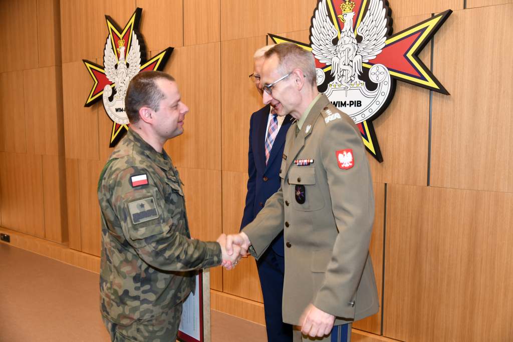 Wojciech Marczyński i Grzegorz Gielerak wręczają dyplom członkowi Rady ubranemu w mundur wojskowy.
