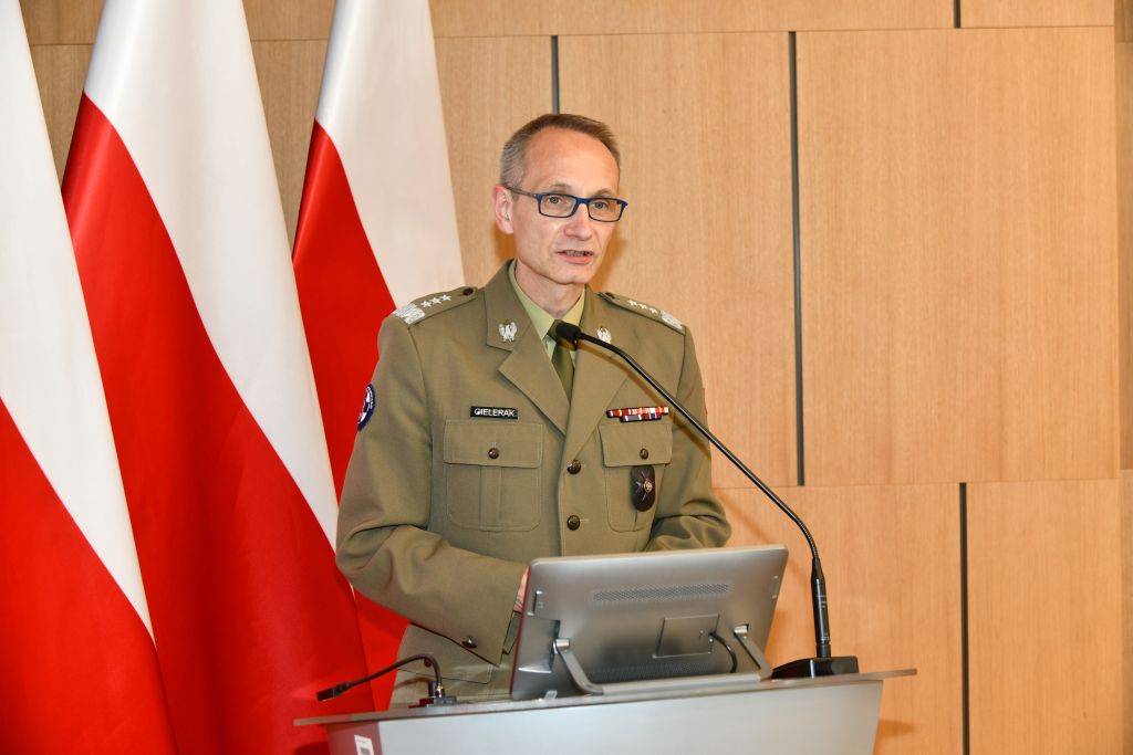 Dyrektor WIM-PIB Grzegorz Gielerak na auli WIM przy mównicy, za nim flagi Polski.