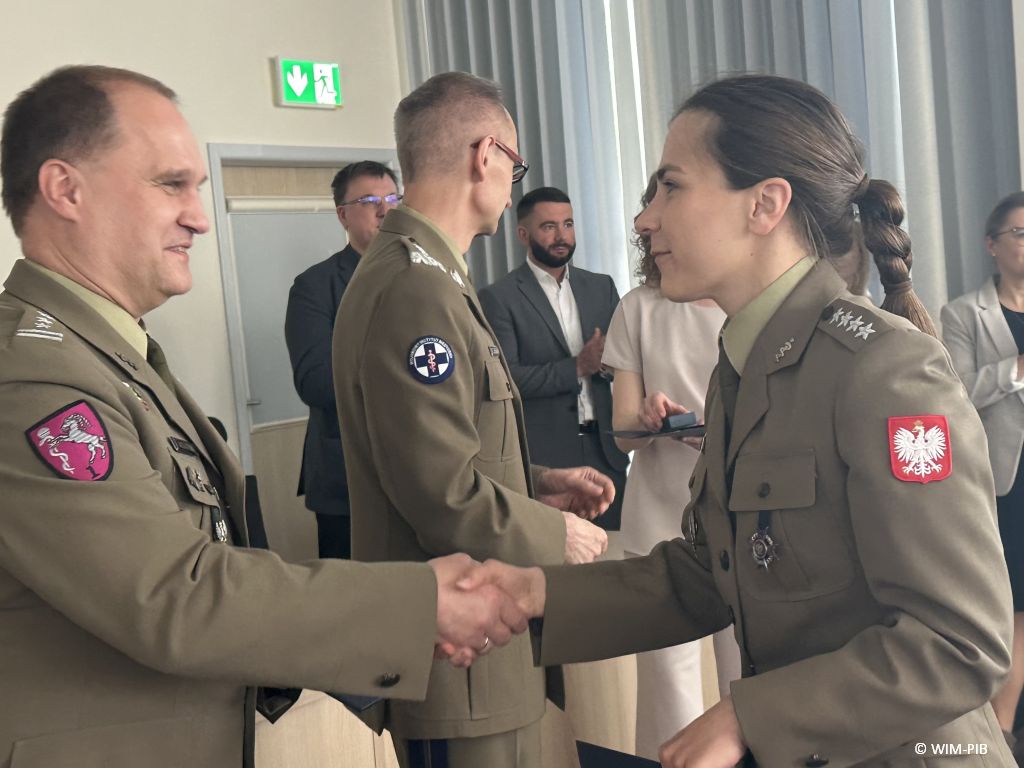 Studentka w mundurze wojskowym ściska rękę pracownikowi WIM-PIB ubranemu w wojskowy mundur.
