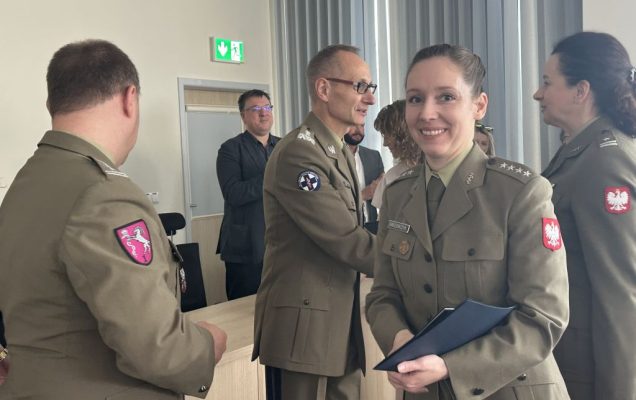 Uśmiechnięta studentka ubrana w wojskowy mundur z dyplomem w rękach.