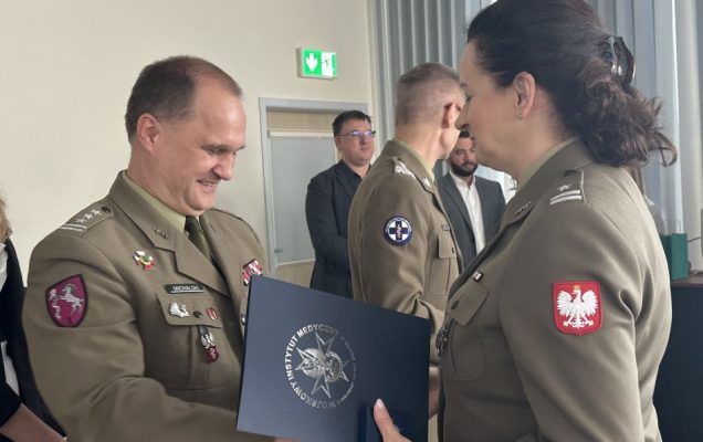 Pracownik WIM-PIB wręcza dyplom studentce ubranej w wojskowy mundur.