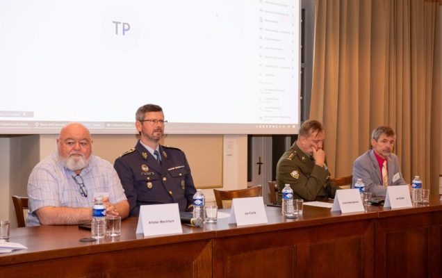 Uczestnicy konferencji przy stole konferencyjnym, za ich plecami wyświetlona prezentacja.