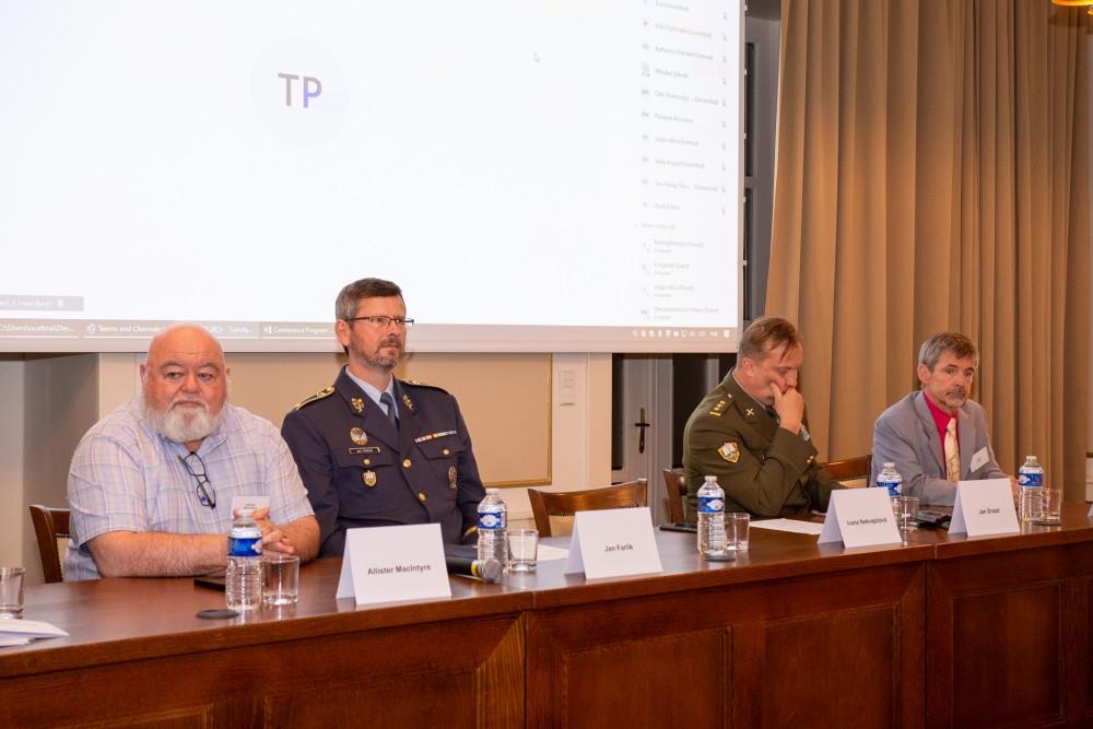 Uczestnicy konferencji przy stole konferencyjnym, za ich plecami wyświetlona prezentacja.