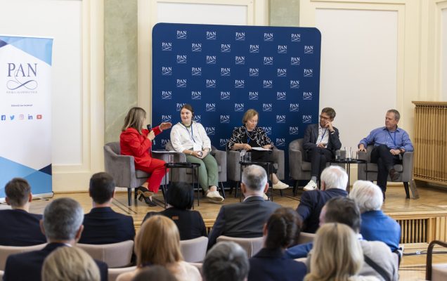 Panel dyskusyjny konferencji, siedzący prelegenci z animi tablica z logotypami PAN.