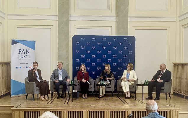 Panel dyskusyjny konferencji, siedzący prelegenci z animi tablica z logotypami PAN.