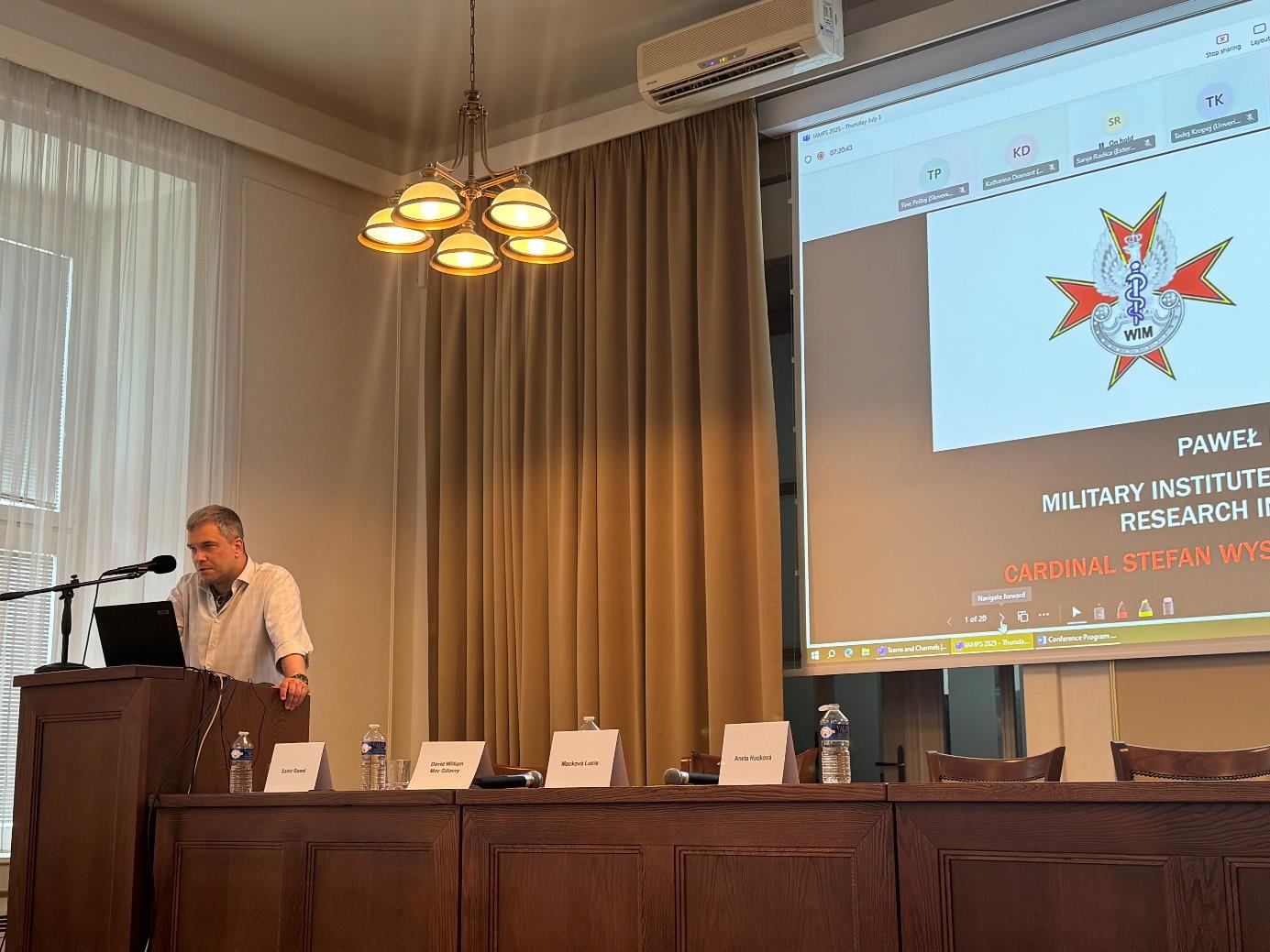 Prelegent podczas wykładu na konferencji. Za jego plecami wyświetlona prezentacja a na niej logo WIM.