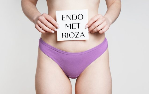 Kadr brzycha młodej kobiety w fioletowych majtkach, trzymającej przed sobą napis endometrioza.