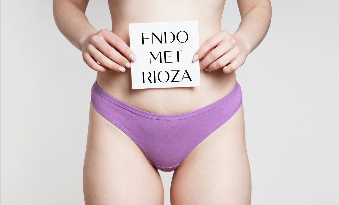 Kadr brzycha młodej kobiety w fioletowych majtkach, trzymającej przed sobą napis endometrioza.