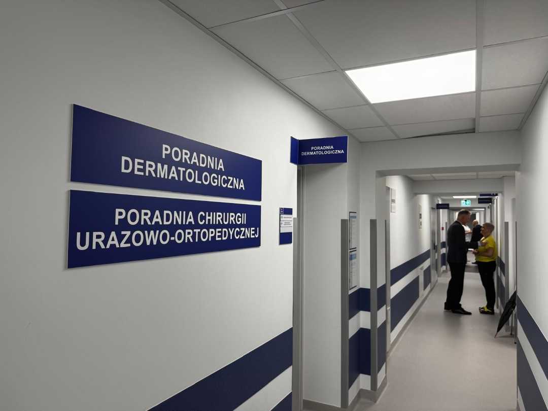 Korytarz poradni. Na ścianie wiszą tablice Poradni dermatologicznej i Poradni Chirurgii Urazowo Ortopedycznej.