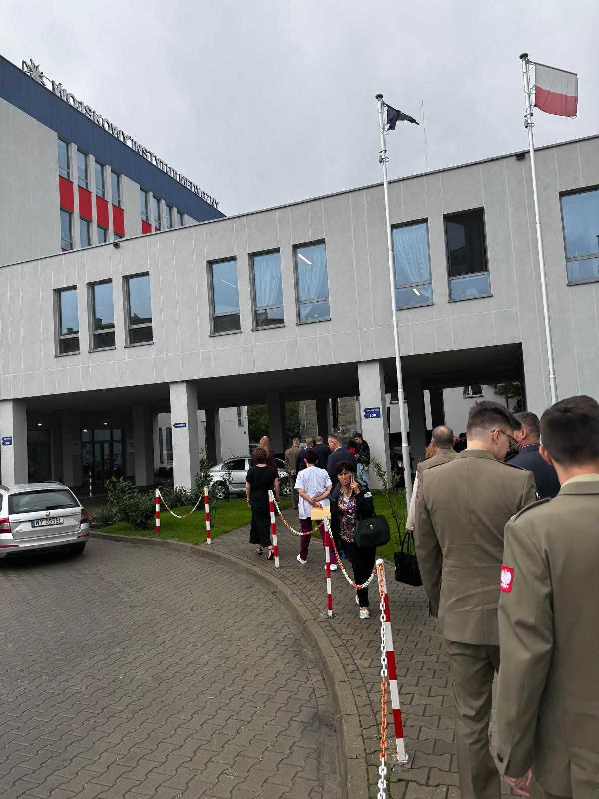 Goście cywilni i mundurowi idą w stronę budynku poradni.