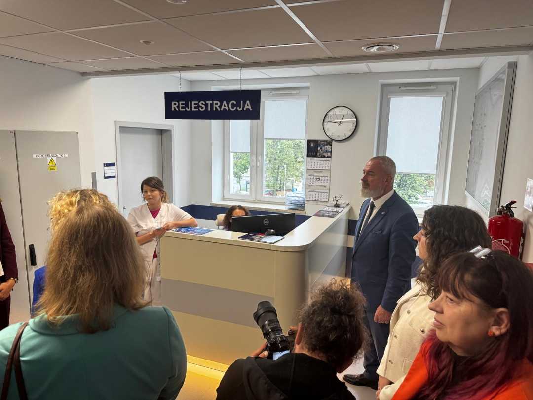 Rejestracja Poradni specjalistycznych w Legionowie. Goście i reporterzy przy kontuarze rejestracji.
