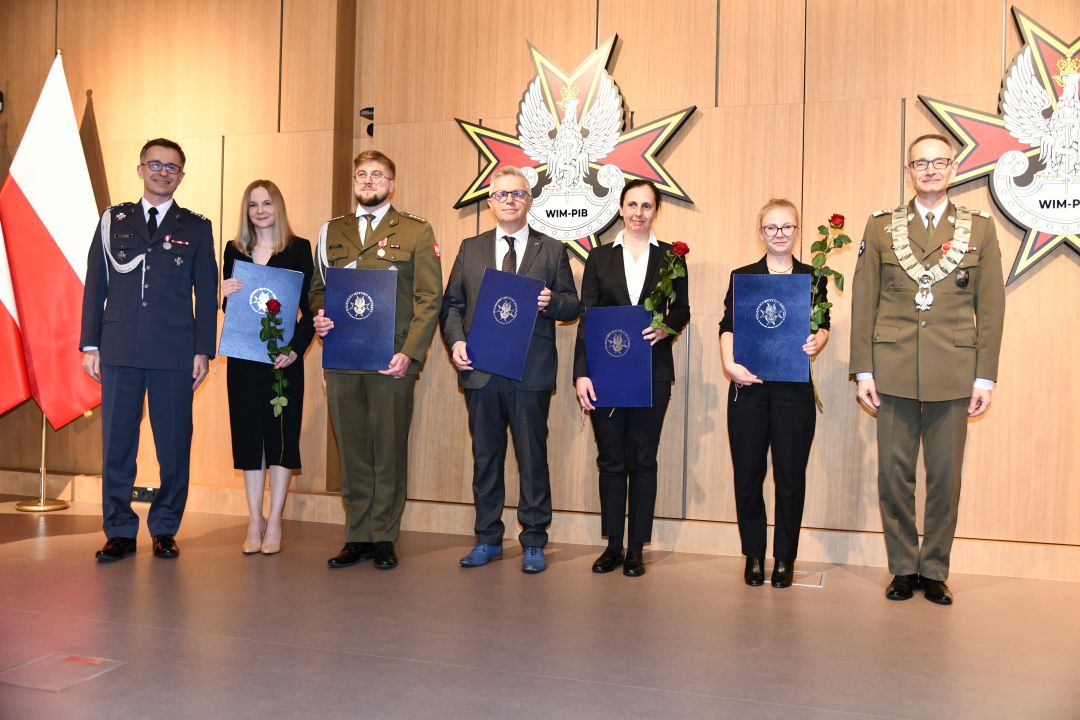 Laureaci z dyplomami pozują do zdjęcia z Dyrektorem WIM, zdjęcie grupowe. Od lewej: Paweł Krzesiński, Marta Mielniczuk, Paweł Rozbicki, Hubert Burdziak, Małgorzata Gajewska, Wanesa Wilczyńska, Grzegorz Gielerak.