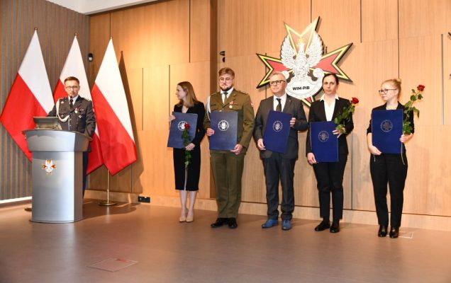 Laureaci z dyplomami pozują do zdjęcia grupowego. Przy mównicy Paweł Krzesiński,. Od lewej: Marta Mielniczuk, Paweł Rozbicki, Hubert Burdziak, Małgorzata Gajewska, Wanesa Wilczyńska.