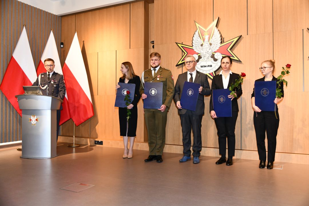 Laureaci z dyplomami pozują do zdjęcia grupowego. Przy mównicy Paweł Krzesiński,. Od lewej: Marta Mielniczuk, Paweł Rozbicki, Hubert Burdziak, Małgorzata Gajewska, Wanesa Wilczyńska.