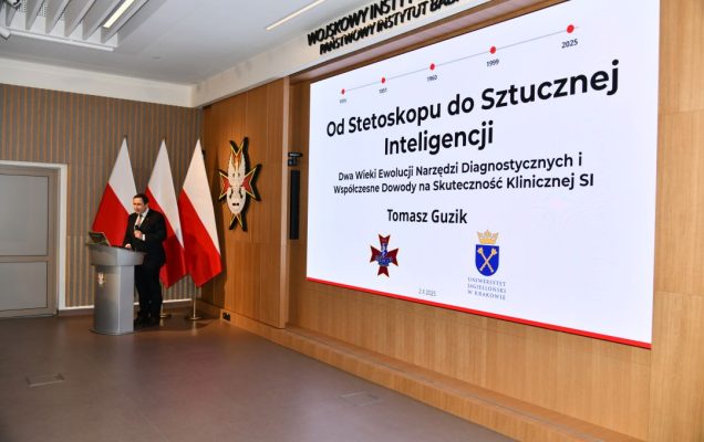 Aula WIM, przy mównicy Prof. dr hab. n. med. Tomasz Guzik, za nim wyświetlony na ekranie tytuł wykładu 