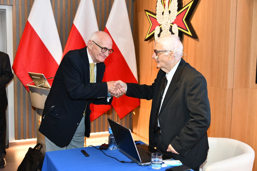 Dwóch prelegentów ściska sobie dłonie.
