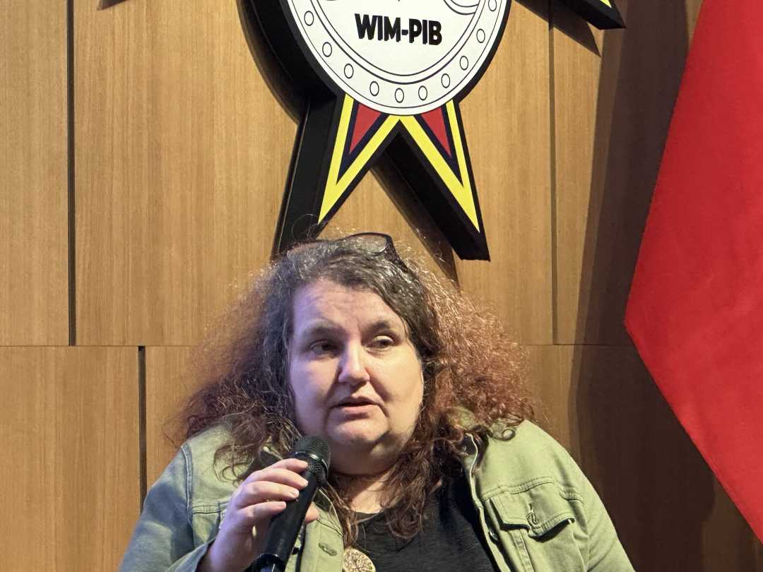 Prelegentka z mikrofonem w dłoni siedzi w fotelu podczas dyskusji panelowej. Za jej plecami fragment wyświetlanej prezentacji.