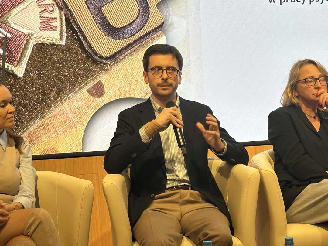 Prelegent podczas panelu. Mężczyzna siedzi w fotelu mówiąc do mikrofonu.