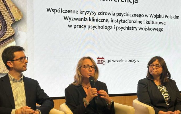 Dwie kobiety i mężczyzna podczas panelu dyskusyjnego siedzą w fotelach. Kobieta w środkowym fotelu mówi do mikrofonu. Za ich plecami na wyświetlaczu tytuł konferencji.