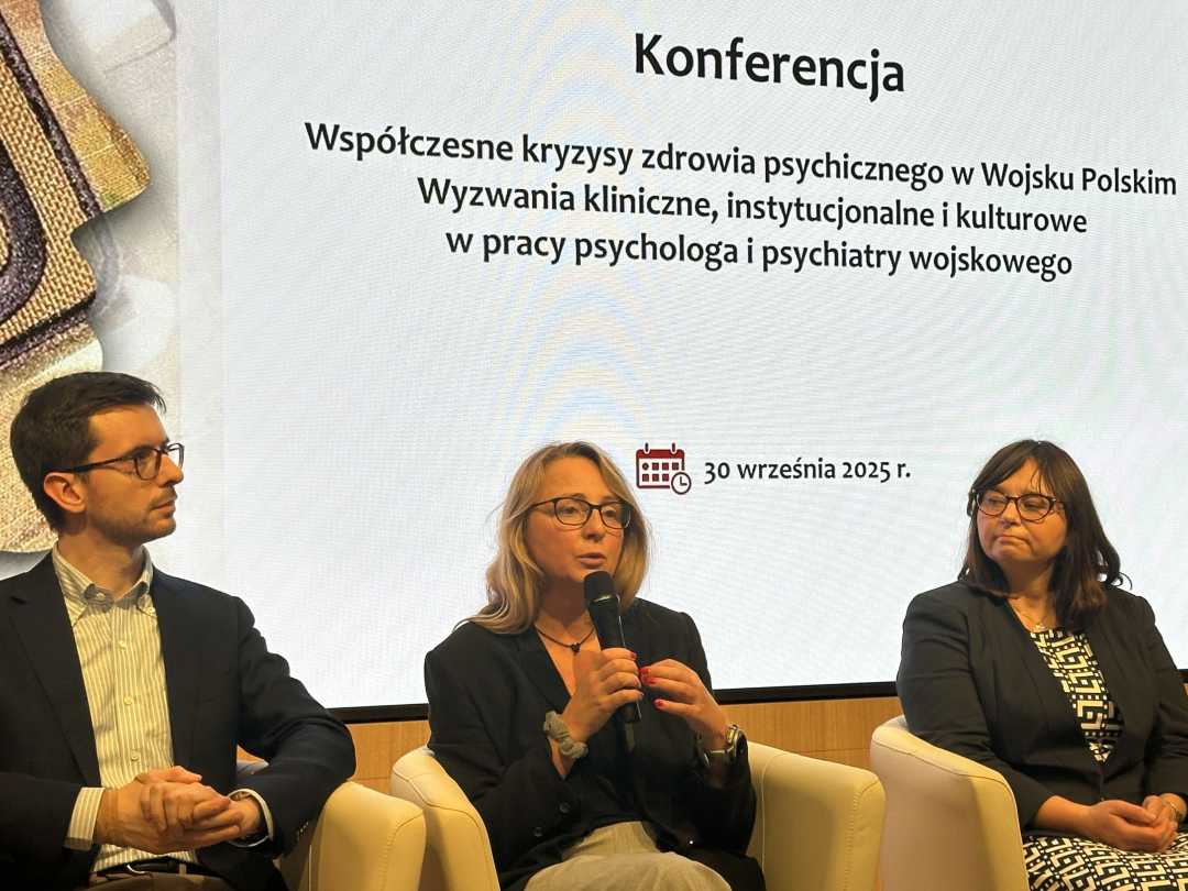 Dwie kobiety i mężczyzna podczas panelu dyskusyjnego siedzą w fotelach. Kobieta w środkowym fotelu mówi do mikrofonu. Za ich plecami na wyświetlaczu tytuł konferencji.