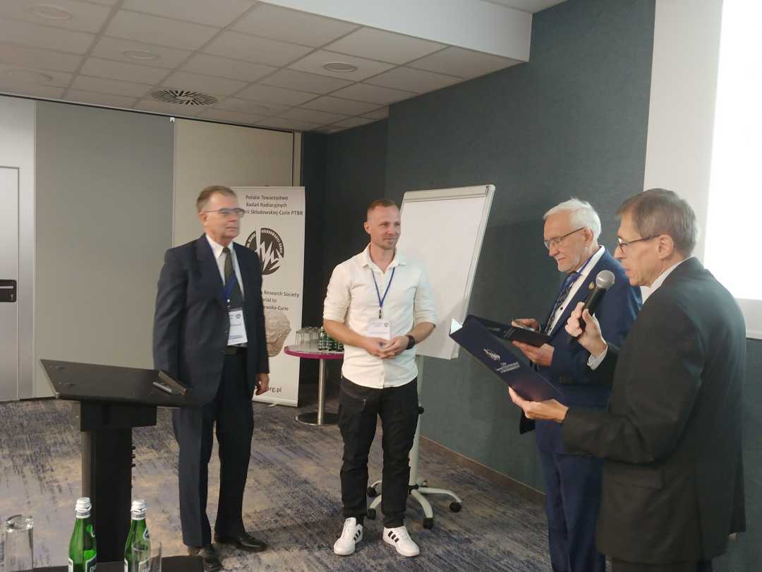 Sala konferencyjna. Prowadzący wydarzenie i laureaci chwilę przed wręczeniem nagrody.