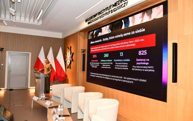 Prelegent przy mównicy za nim na wyświetlaczu fragment prezentacji.