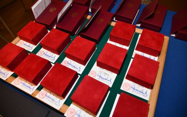 Odznaki w czerwonych aksamitnych pudełkach ułożone obok siebie na stole z niebieskim płótnem.