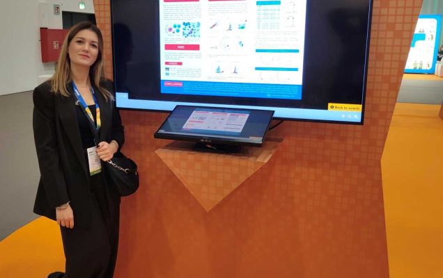 Alicja Dudzik stoi przy wyświetlaczu z plakatem w holu konferencyjnym.