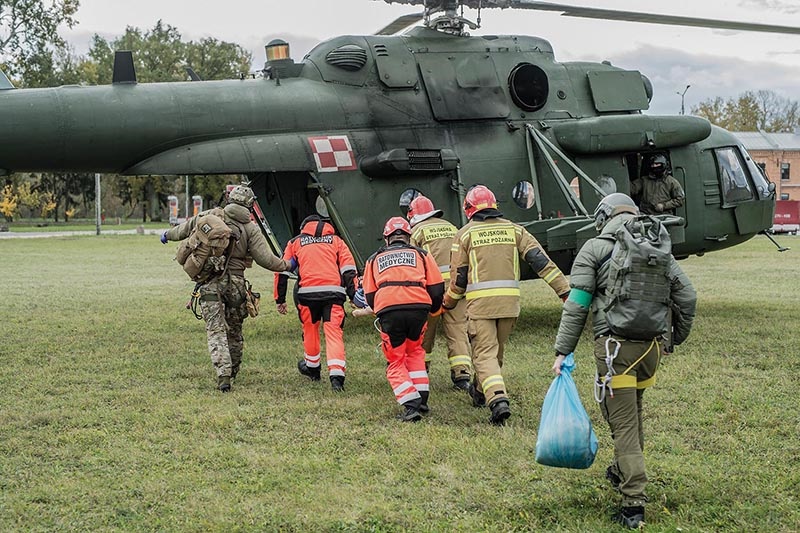 Symulacja bojowa, żołnierze i ratownicy  kierują się w stronę wojskowego helikoptera.