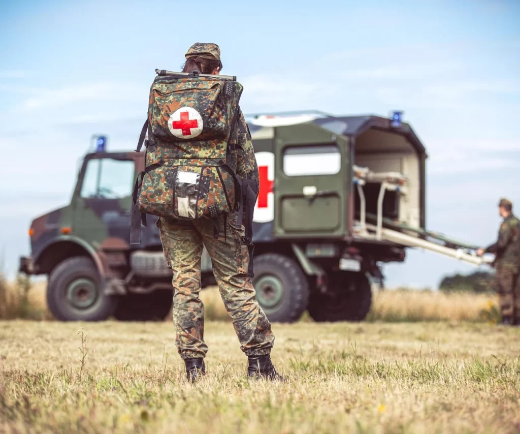 Żołnierz w stroju polowym przed nim ambulans ratowniczy.