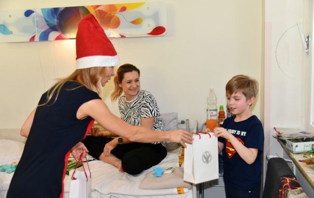 Małgorzata Złotkowska w czapce świętego Mikołaja wręcza prezent chłopcu.
